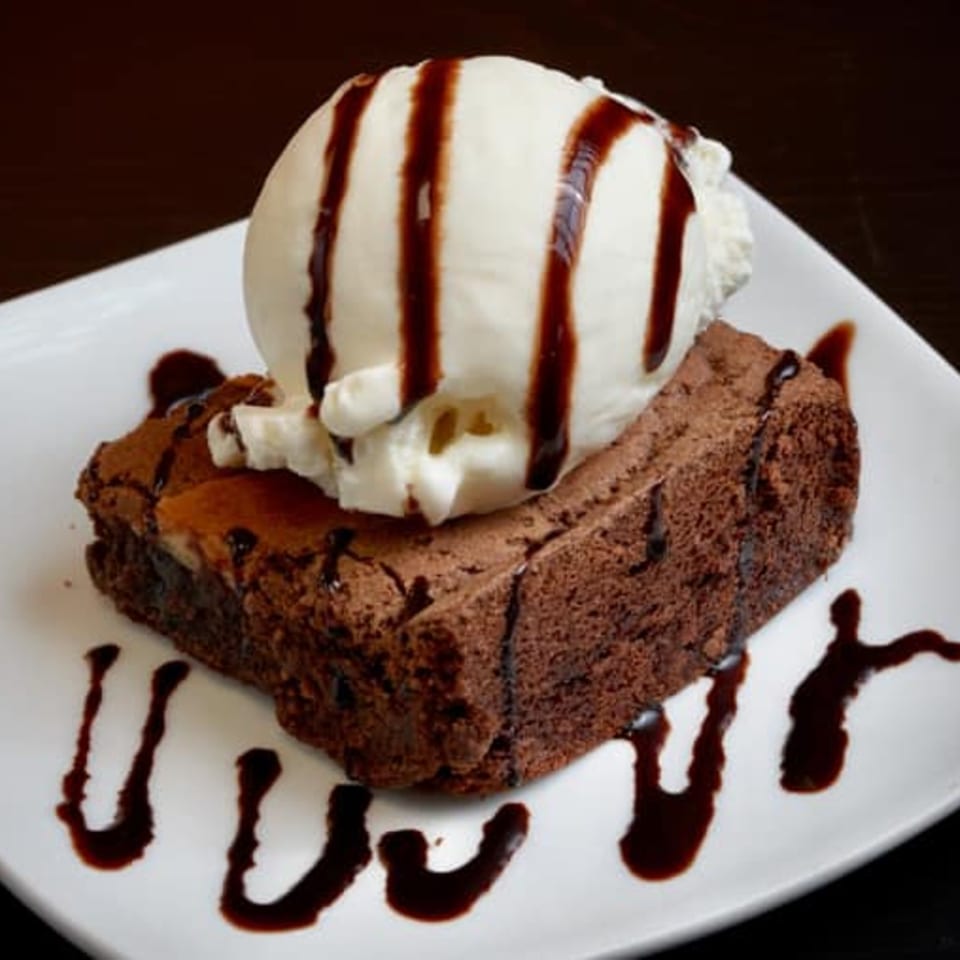 A rich chocolate brownie topped with a scoop of vanilla ice cream and drizzled with chocolate syrup.