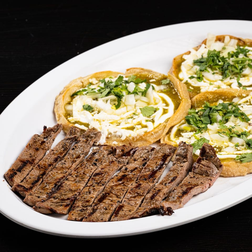 Grilled steak slices and three sopes with green sauce, cheese, and cilantro on a white plate.