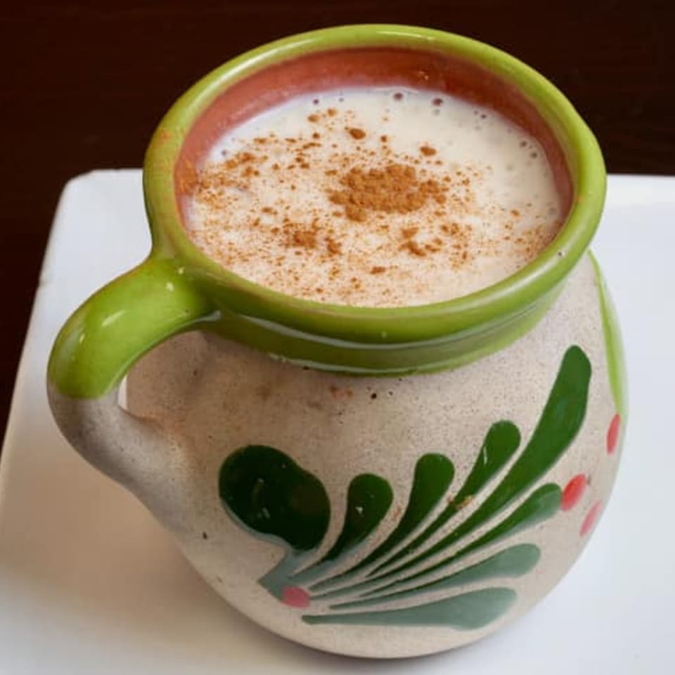 Horchata in a traditional green and red painted ceramic mug, sprinkled with cinnamon.